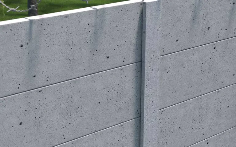 Šedý průmyslový betonový plot s hladkými deskami a ostnatým drátem nahoře
