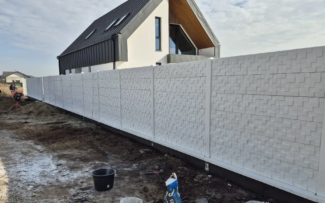 Bílý betonový plot s geometrickým reliéfem před moderním domem